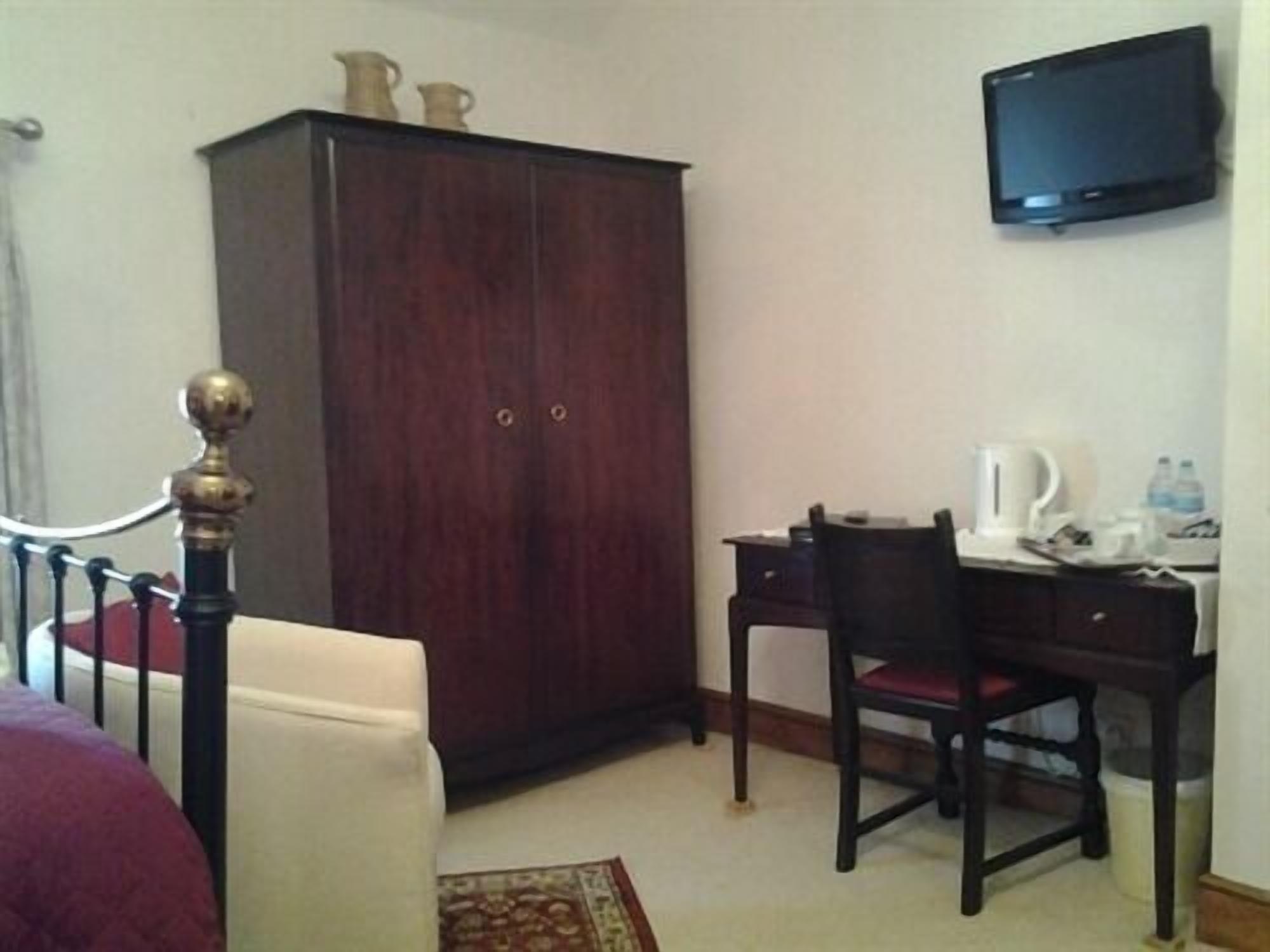 A hotel room with a bed, a wardrobe, a desk with a chair, a television, and a coffee maker.