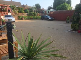 A residential driveway with two cars parked, a wooden bench, and a potted plant in the foreground.