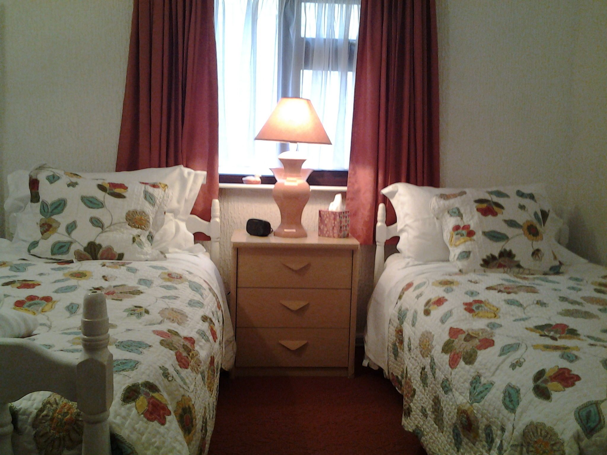 A twin bedroom with floral bedding, a bedside lamp, and a nightstand with a tissue box.