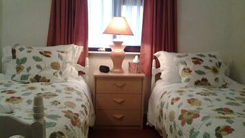 A twin bedroom with floral bedding, a bedside lamp, and a nightstand with a tissue box.