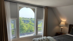 A bedroom with a large arched window, a bed, a nightstand with a lamp, and a small table. - Redwood Bed and Breakfast (Niagara Falls)