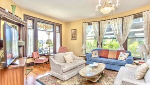 A living room with a wooden floor, a blue sofa, a patterned armchair, a coffee table, and a chandelier. - Redwood Bed and Breakfast (Niagara Falls)