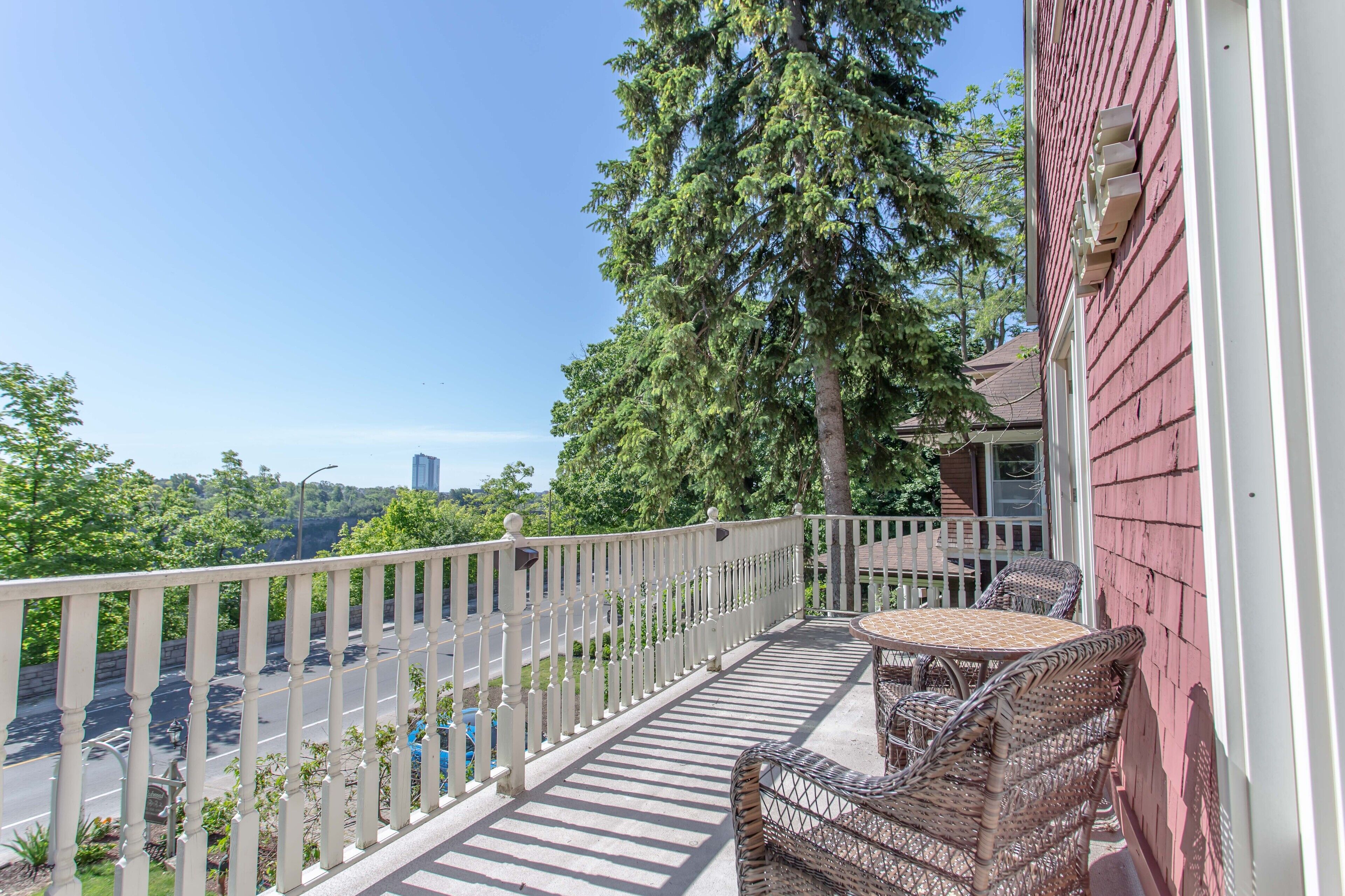 A balcony with wicker furniture, a white railing, and a view of a road and trees.
