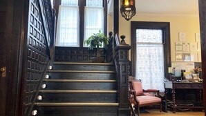 A grand staircase with ornate railings and a chandelier, leading to a room with a desk and a chair. - Redwood Bed and Breakfast (Niagara Falls)