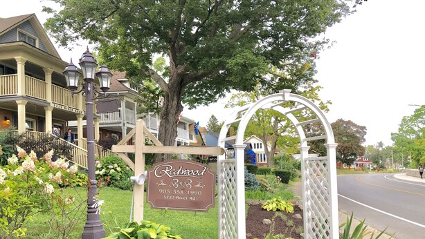 A sign for Redwood B&B at 5227 River Rd. with a garden entrance and a white lattice archway. - Redwood Bed and Breakfast (Niagara Falls)