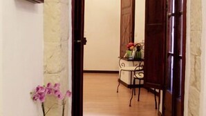 A hallway with a stone archway leading to a room with a wooden door and a small table with a vase of flowers. - Cagliari Castello Affittacamere (Cagliari)