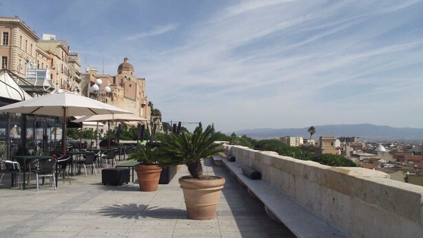 An outdoor terrace with tables and chairs, potted plants, and a view of historic buildings. - Cagliari Castello Affittacamere (Cagliari)