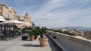 An outdoor terrace with tables and chairs, potted plants, and a view of historic buildings. - Cagliari Castello Affittacamere (Cagliari)