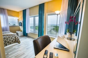 Habitación de hotel con cama, escritorio con una computadora portátil, una silla, televisor y vistas a la carretera y áreas verdes.