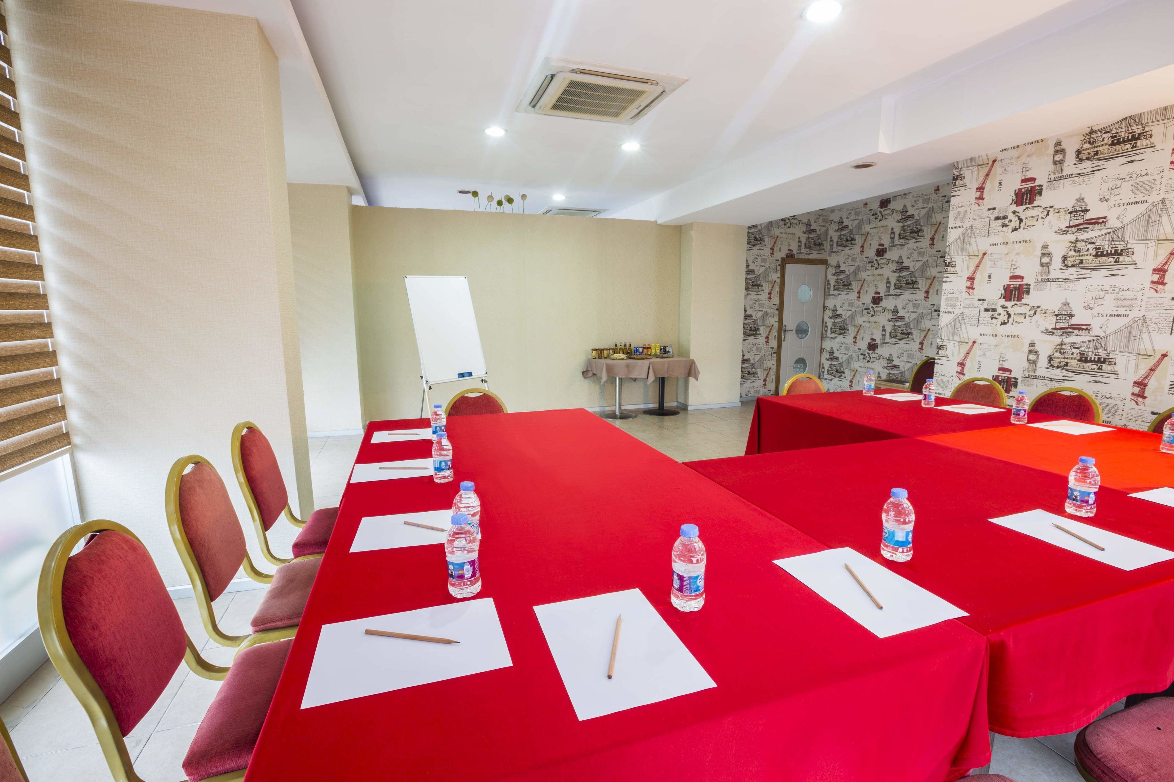 Uma sala de conferências com mesas, cadeiras e garrafas de água, tudo em vermelho.