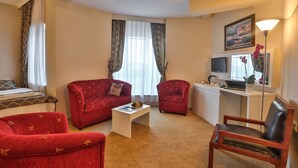 A hotel room with a bed, two red sofas, a coffee table, a desk with a computer, a chair, and a TV. - Arsen Hotel (Arsin)
