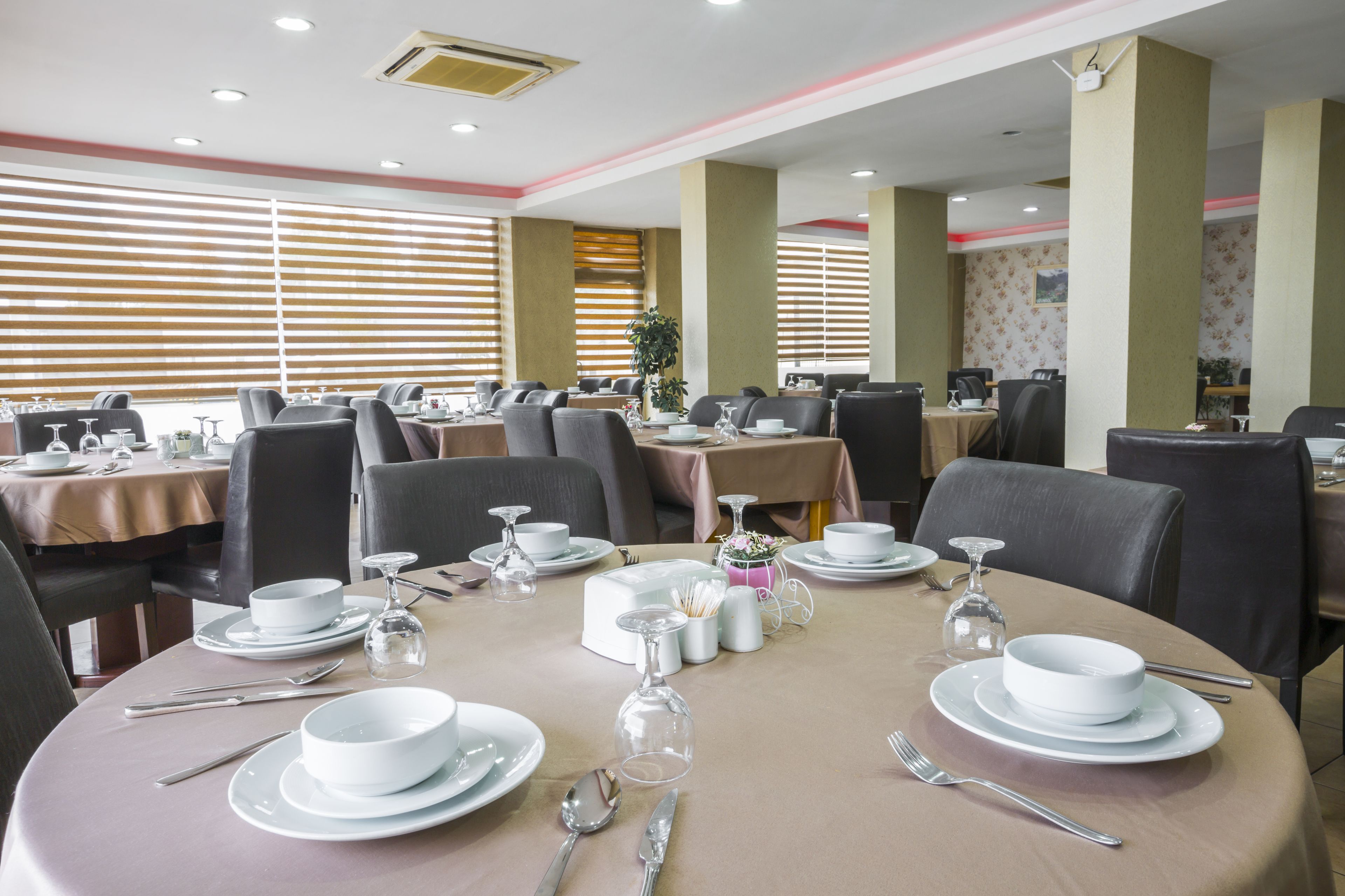 A dining area with round tables set for service, equipped with white tablecloths, plates, cutlery, and glassware.