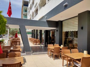 An outdoor patio area with wooden tables and chairs, a flag, and a building entrance.