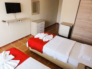 A hotel room with two beds, a TV, a mirror, a small cabinet, and a red and white towel on each bed.