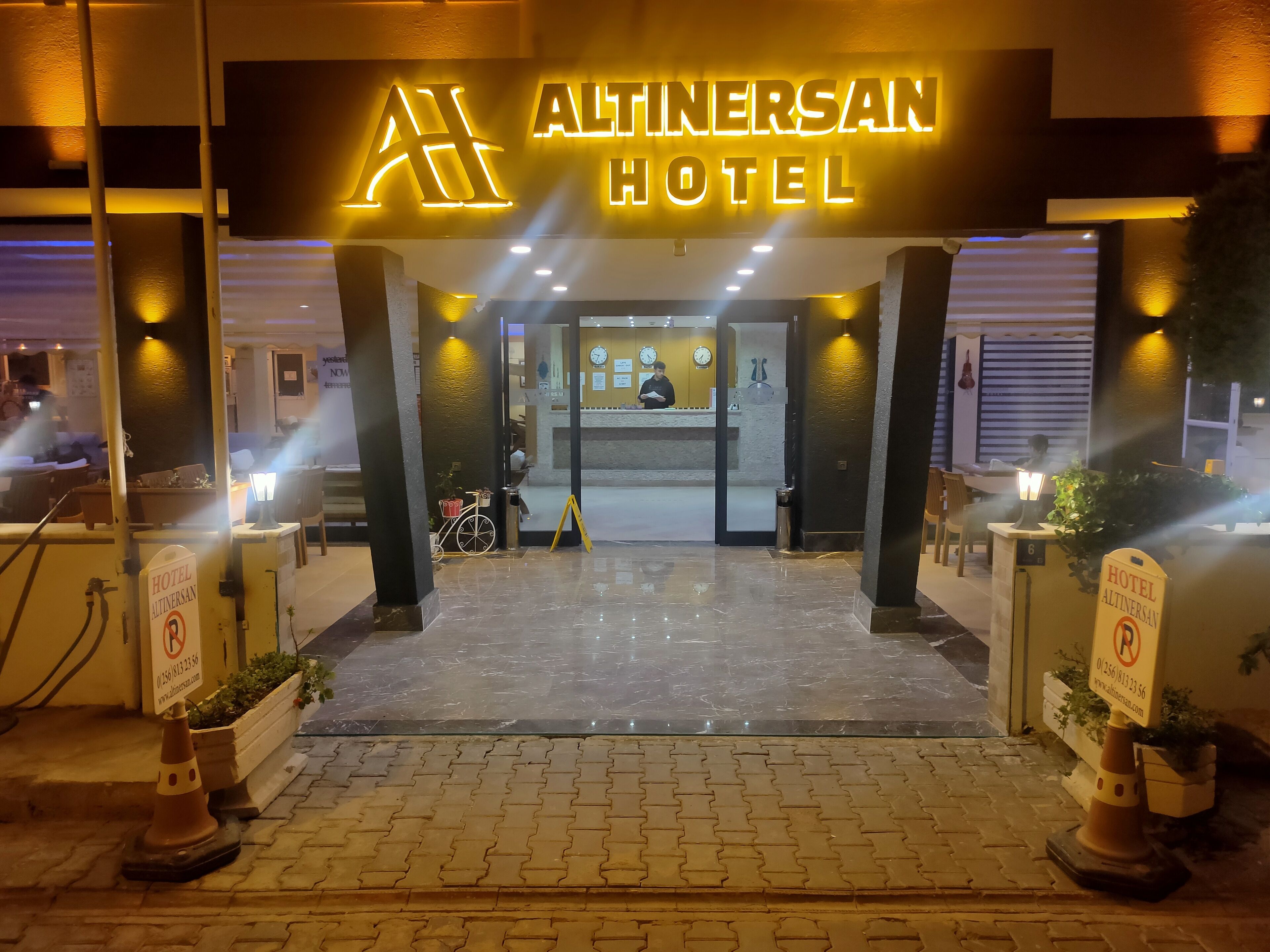 The entrance to Altinversan Hotel with a reception desk, a bicycle, and a sign indicating the hotel's name.