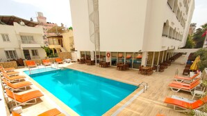Ein Poolbereich auf dem Dach mit orangefarbenen Liegestühlen und Tischen, umgeben von einem Gebäude mit mehreren Balkonen und einer Wendeltreppe.