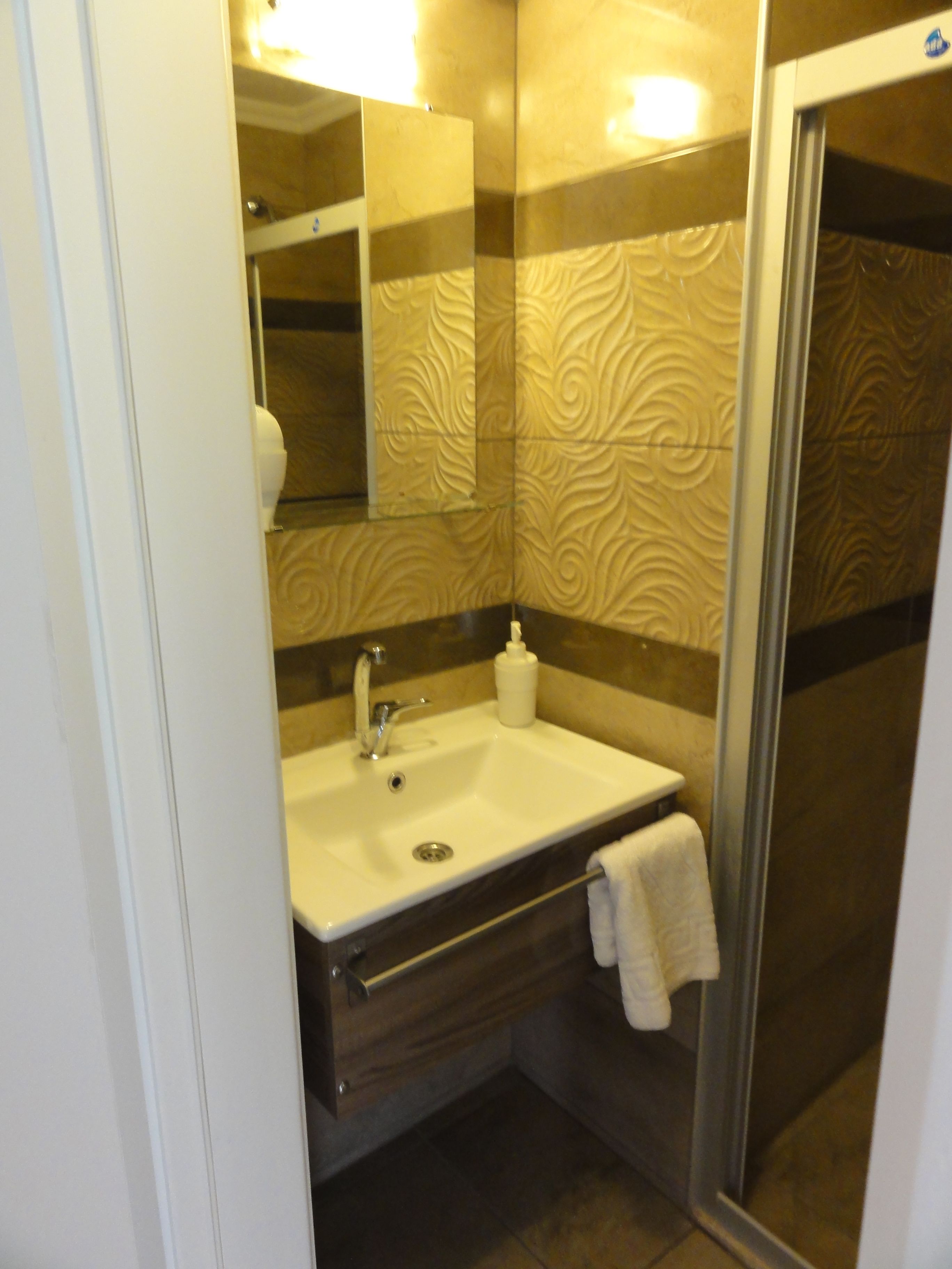 Un baño con lavamanos blanco, espejo, toalla y zona de ducha.