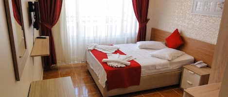 A hotel room with a bed, a bedside table, a nightstand, a wall-mounted phone, and a window with curtains.