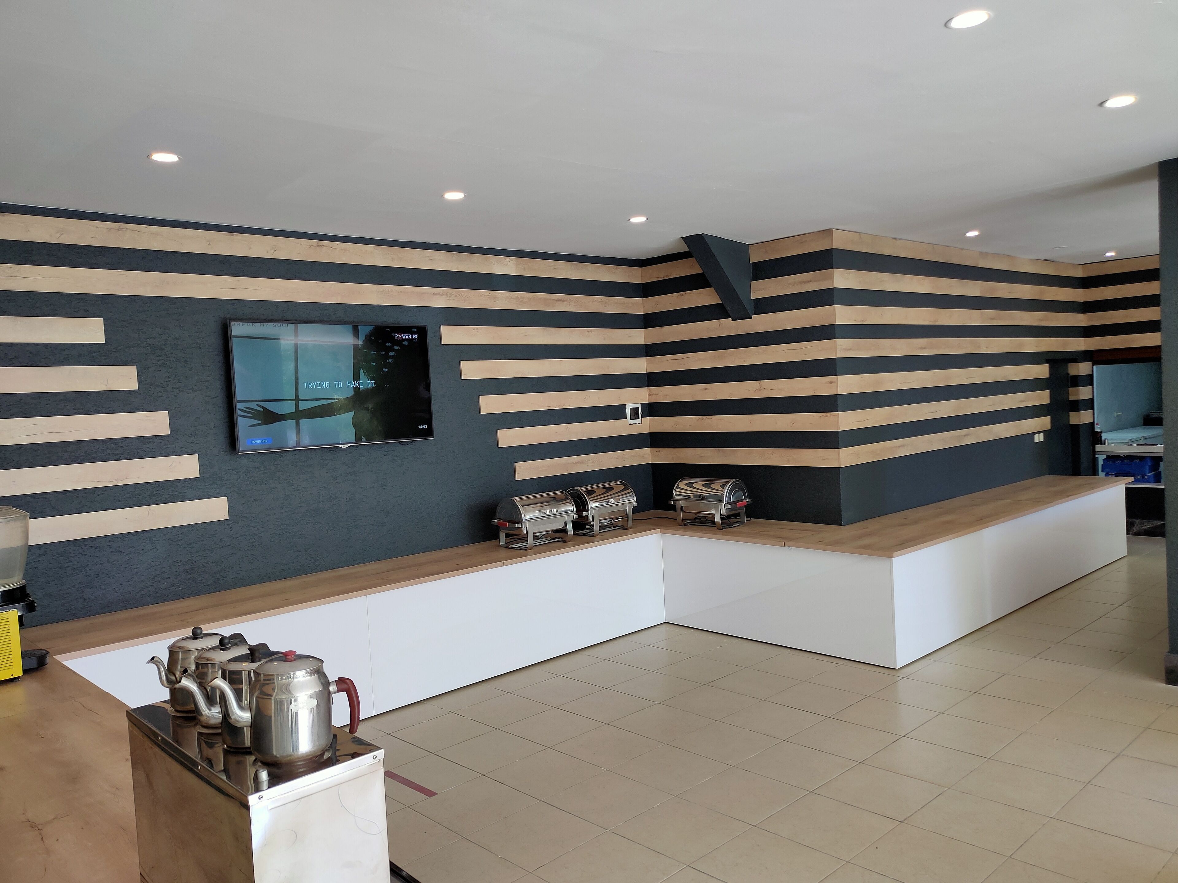 A modern reception area with a flat-screen TV mounted on the wall, a wooden counter, and a coffee station with kettles and a coffee pot.