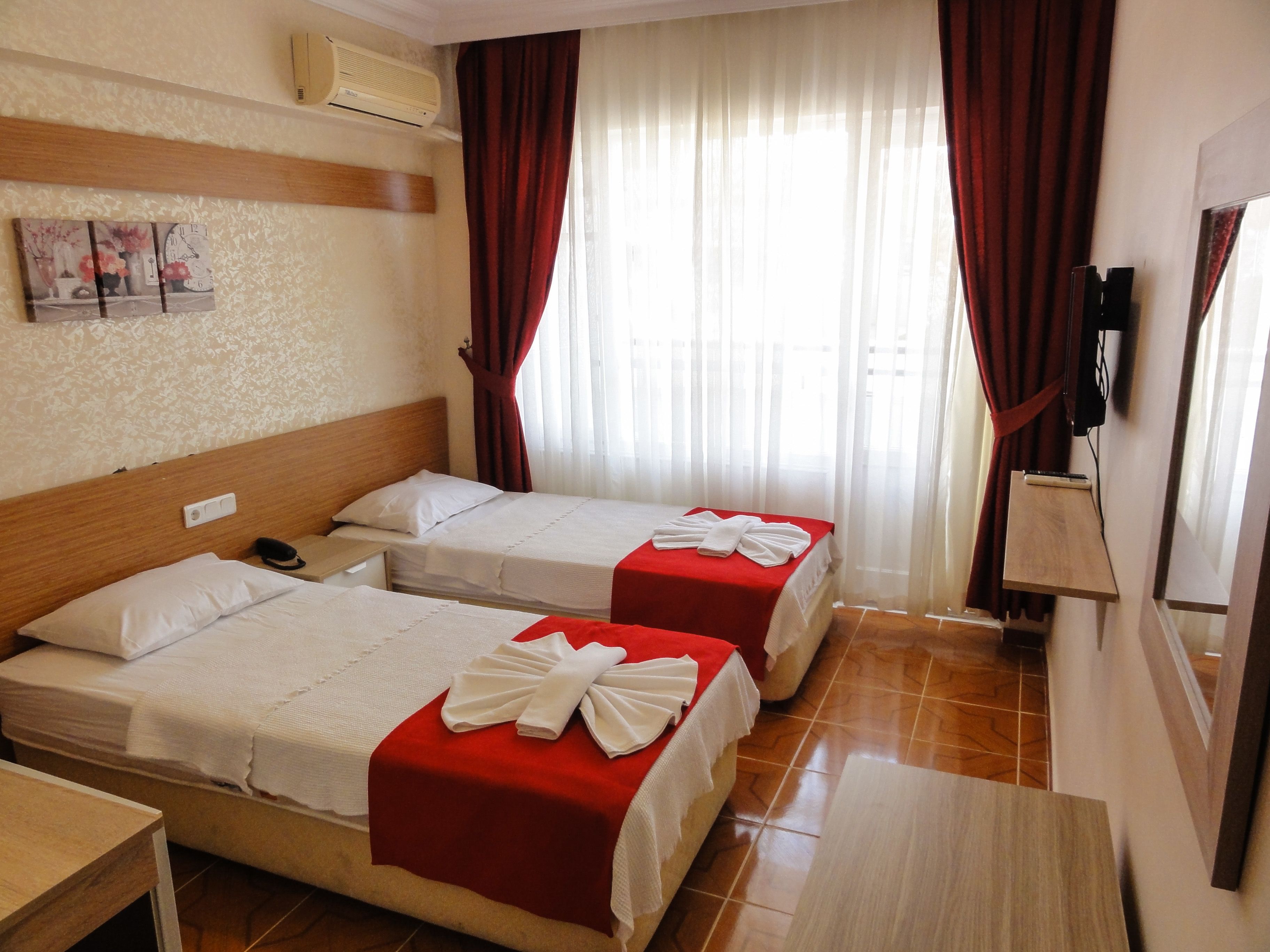 Habitación de hotel con dos camas, cabecero de madera, una mesita, televisor y ventana con cortinas.