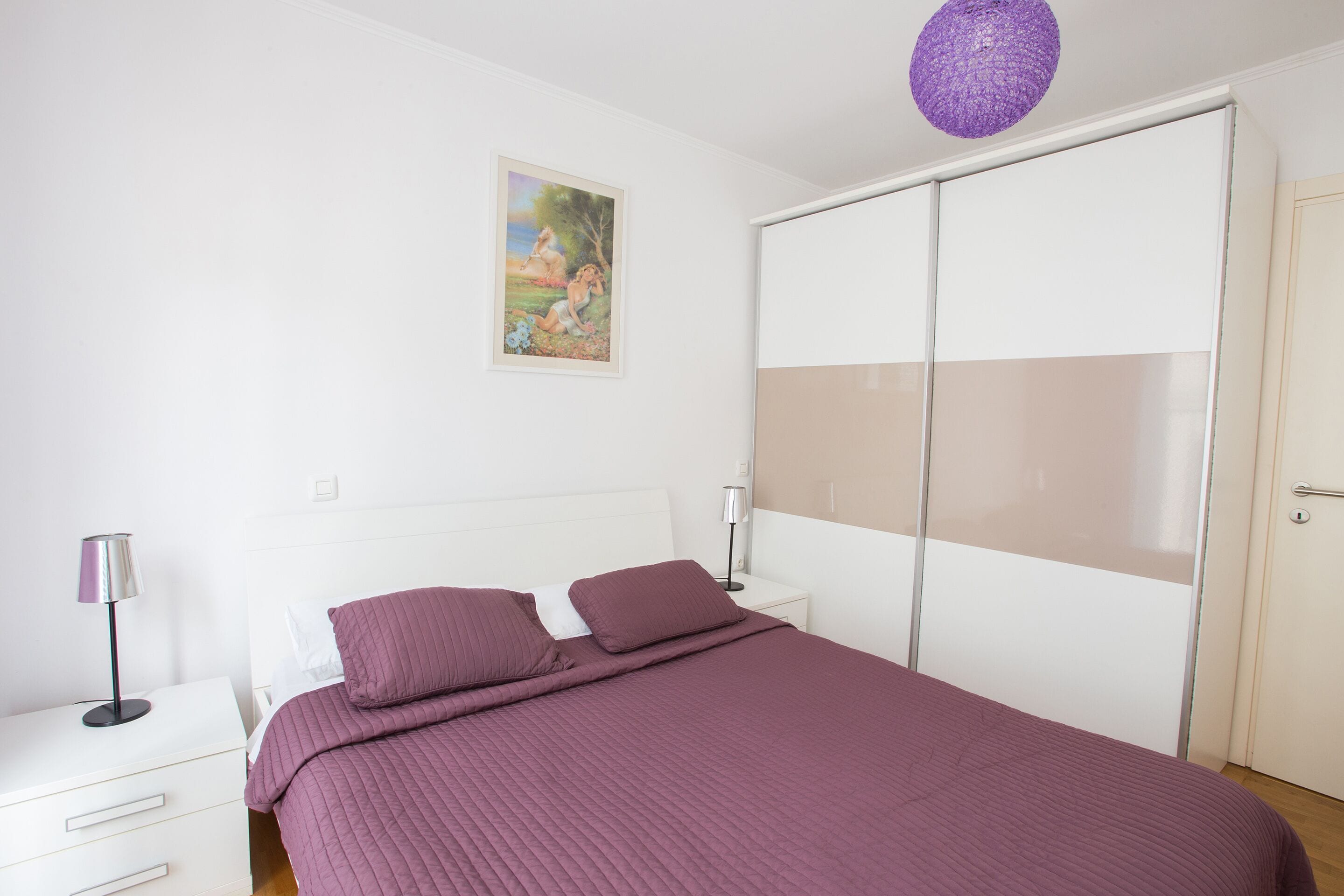 Un dormitorio con cama, mesitas de noche, cómoda, armario y un cuadro en la pared.
