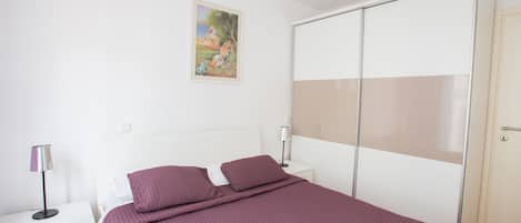 Un dormitorio con cama, mesitas de noche, cómoda, armario y un cuadro en la pared.
