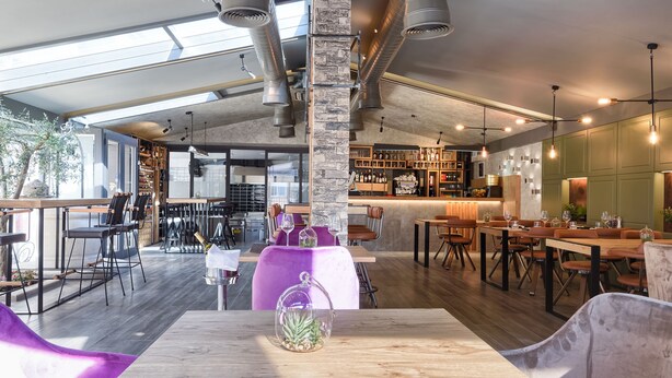 Un restaurant moderne avec de hauts plafonds, des conduits apparents et un mélange de meubles en bois et de meubles rembourrés.