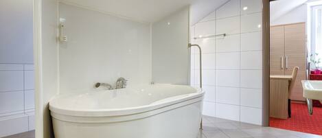 Un baño moderno con una bañera independiente, paredes de azulejos blancos y suelo cubierto de alfombra roja.