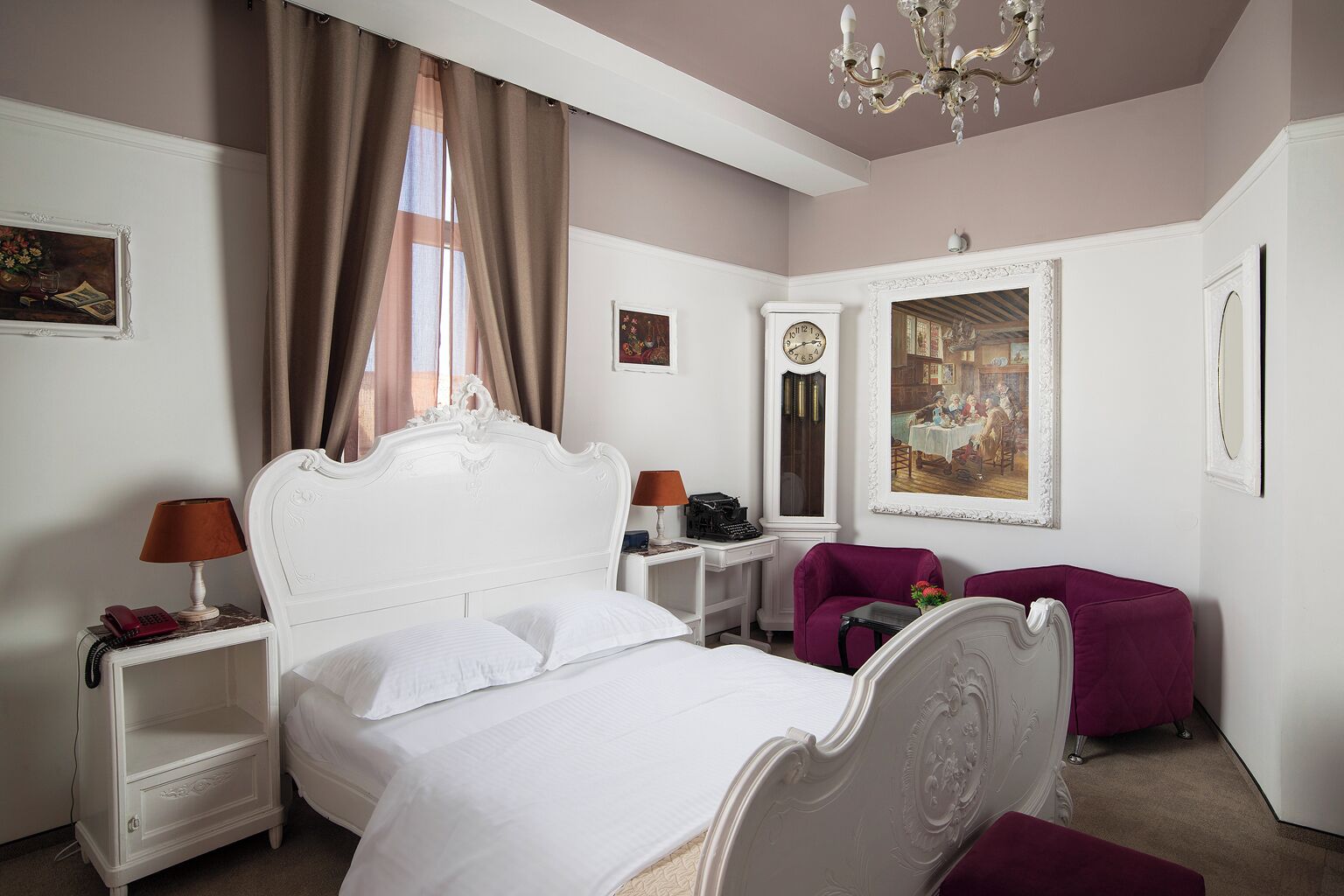 Une chambre à coucher avec un lit blanc, une table de chevet avec une lampe, un fauteuil violet et un tableau accroché au mur.