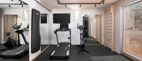 Un gimnasio con cintas de correr, bicicletas estáticas y un espejo grande.