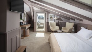 Une chambre aménagée dans les combles, avec un lit, deux fauteuils, un bureau et un téléviseur.