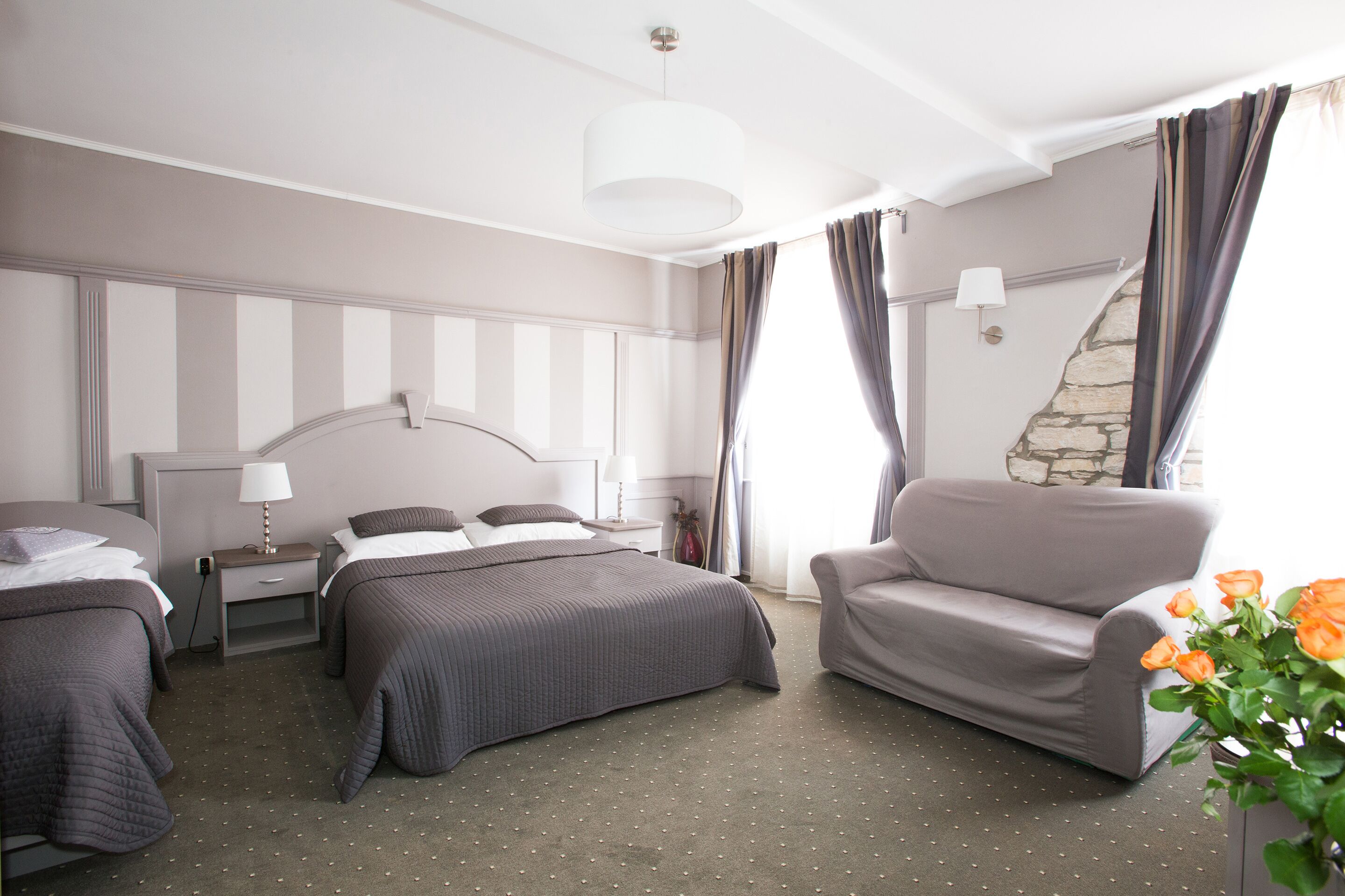 Habitación de hotel con cama, una silla, una mesita de noche, lámpara y ventana con cortinas.