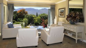 A spacious living area with a view of mountains, a white sofa, a dining table, and a decorative vase. - Alba House Bed & Breakfast (Paarl)