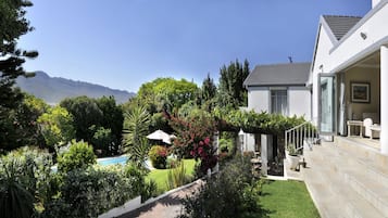 A modern house with a pool, lush garden, and a view of mountains.