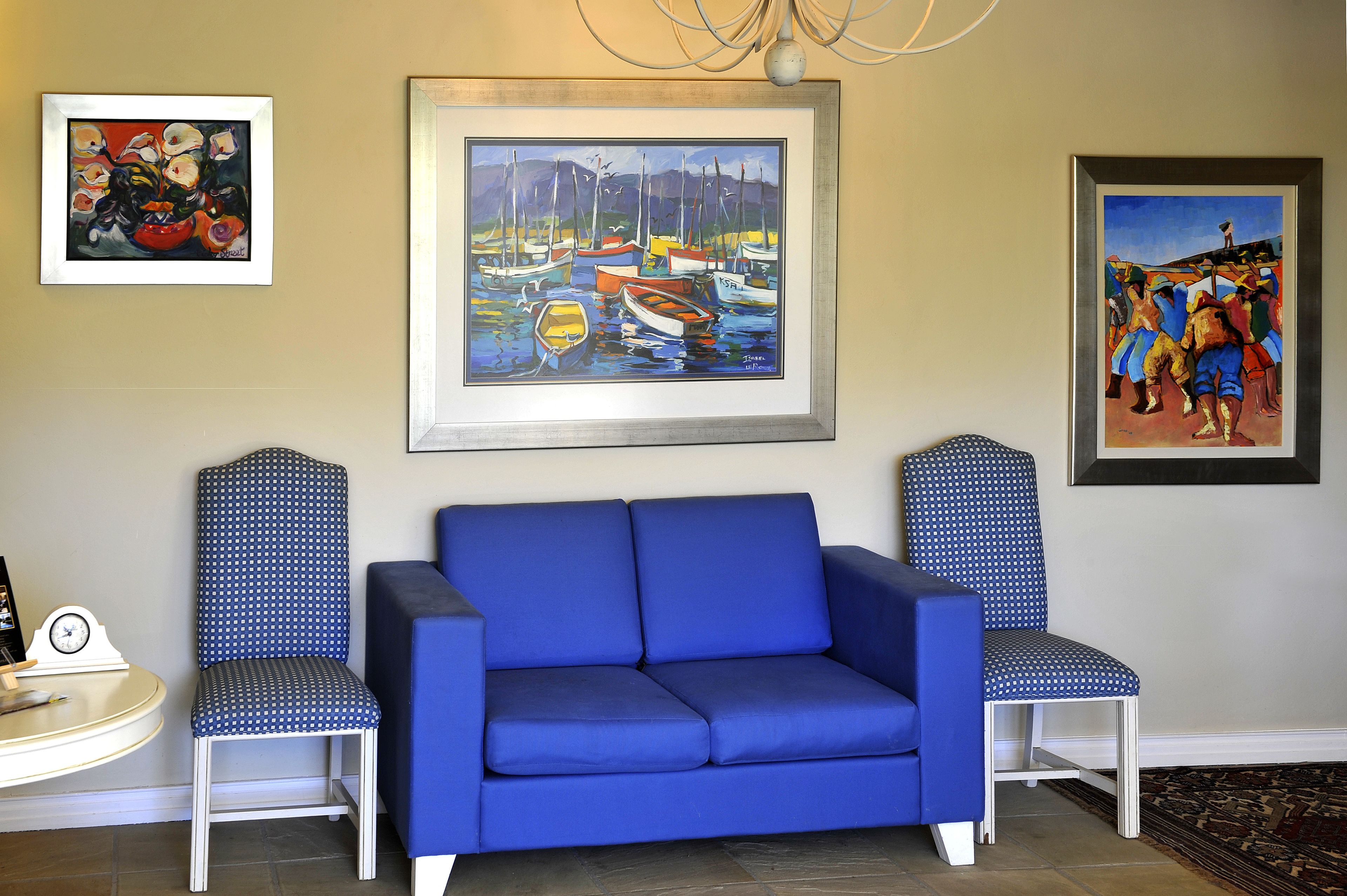 A blue sofa with matching chairs, a framed painting of boats, and a clock on a table.