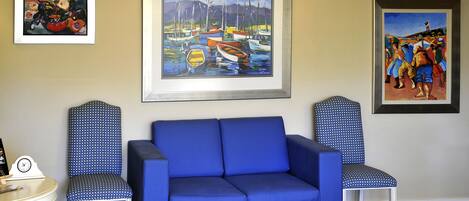 A blue sofa with matching chairs, a framed painting of boats, and a clock on a table.