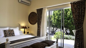 A bedroom with a bed, bedside lamp, and a view of a garden through a sliding door. - Alba House Bed & Breakfast (Paarl)