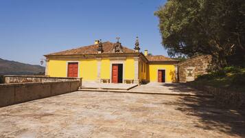 Um edifício amarelo com portas vermelhas, uma parede de pedra e uma grande árvore.