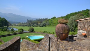 Un área de piscina con paredes de piedra, una gran maceta rústica y un edificio de piedra al fondo.