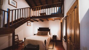 Un dormitorio con escalera de madera, una cama, una silla y una mesita de noche.