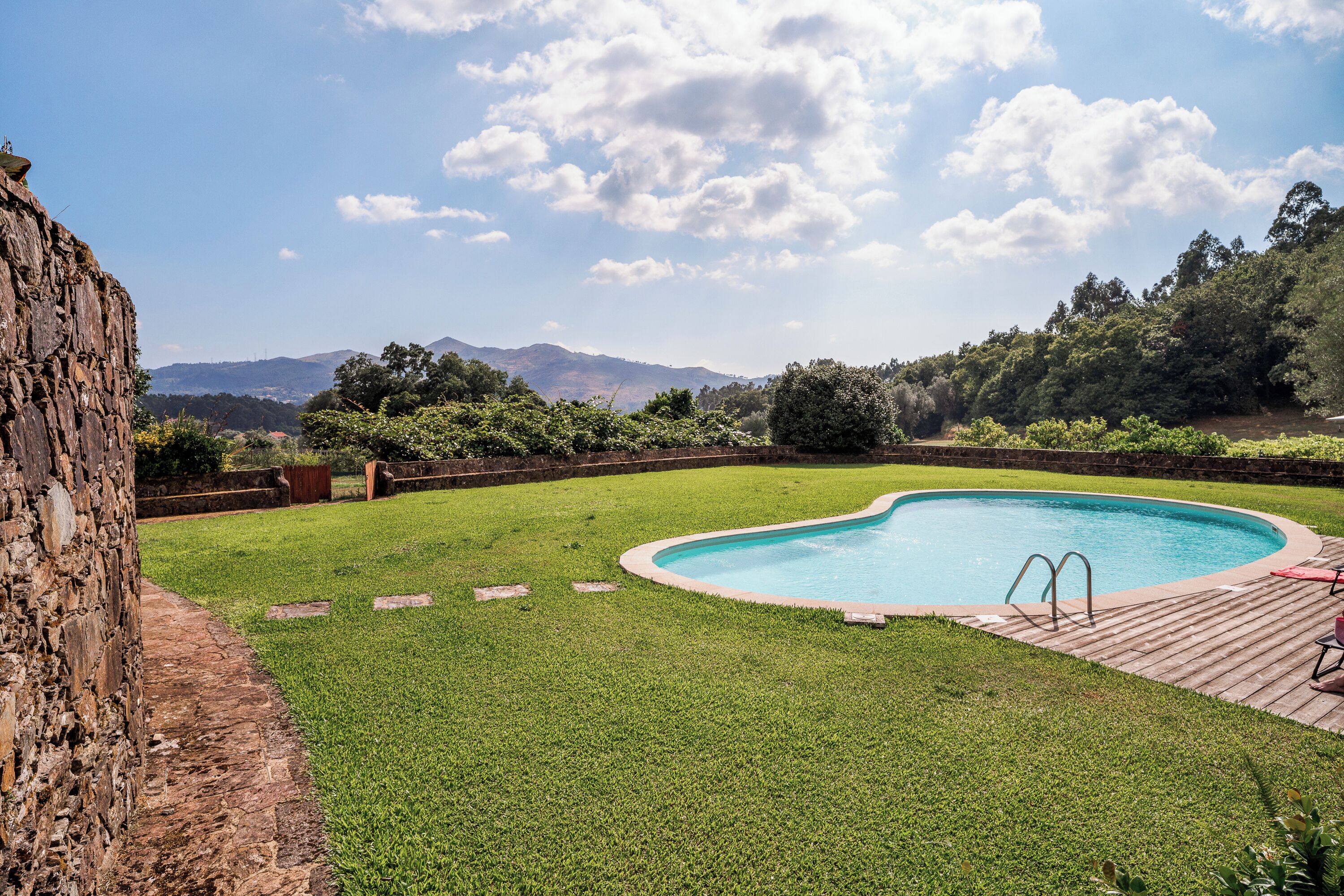 Une piscine dotée d’une terrasse en bois et d’un mur en pierre.