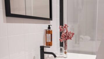 A bathroom with a white sink, black faucet, and a mirror above it. There is a bottle of soap and a vase with flowers on the sink.