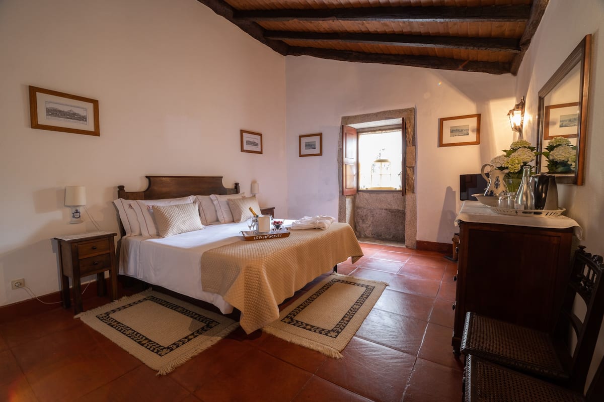 Un dormitorio con cama, mesitas de noche, cómoda, espejo y ventana con vistas.