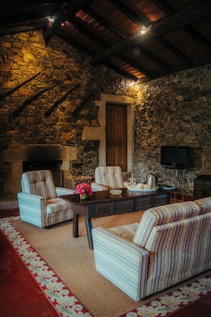 Una habitación acogedora con paredes de piedra, chimenea, muebles tapizados a rayas y televisor.