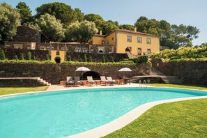 A swimming pool with lounge chairs and umbrellas, surrounded by stone walls and a building with multiple windows. - Casa Do Anquião (Ponte de Lima)