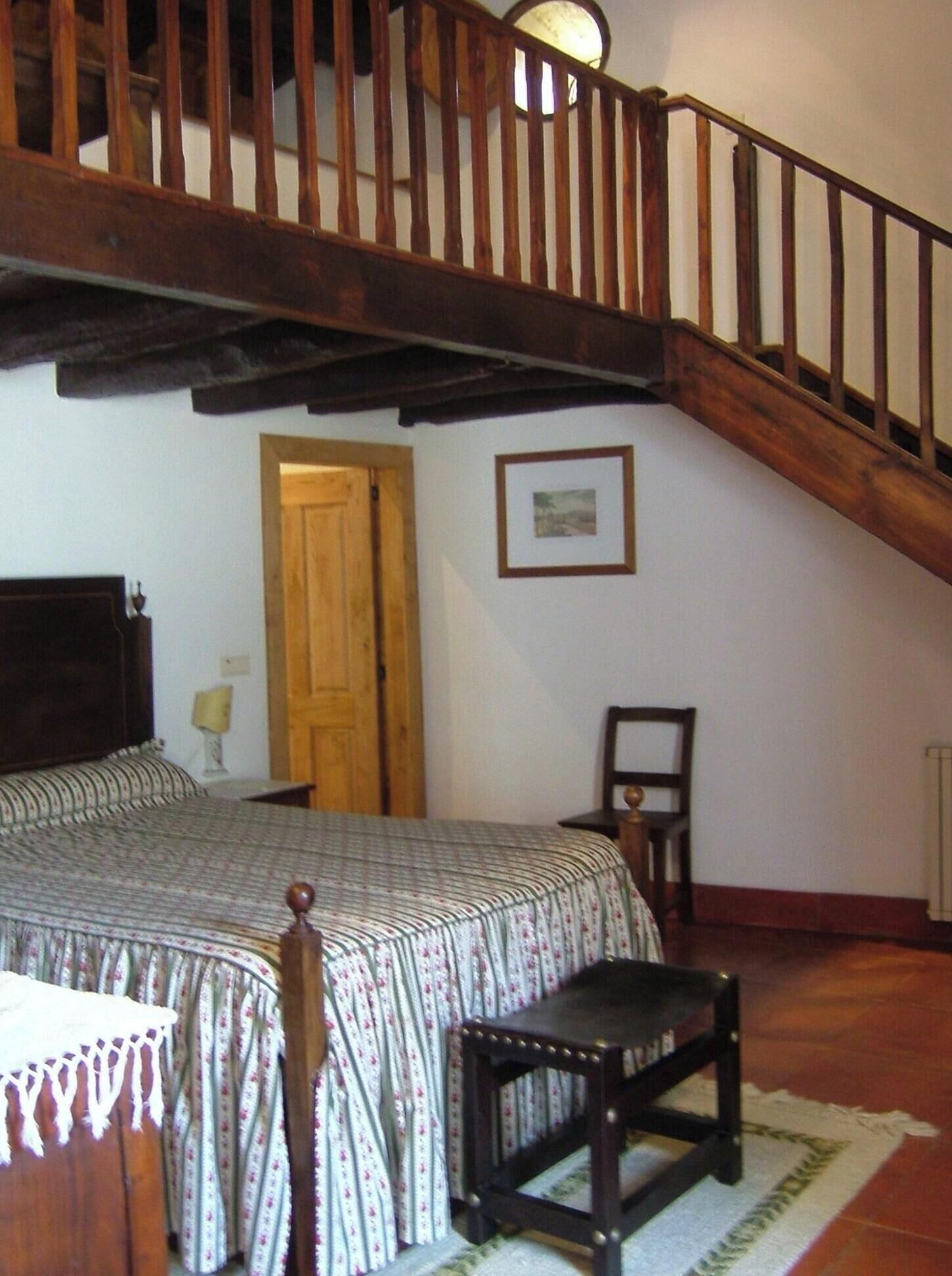 A bedroom with a wooden staircase, a bed with a patterned bedspread, a chair, and a small table.