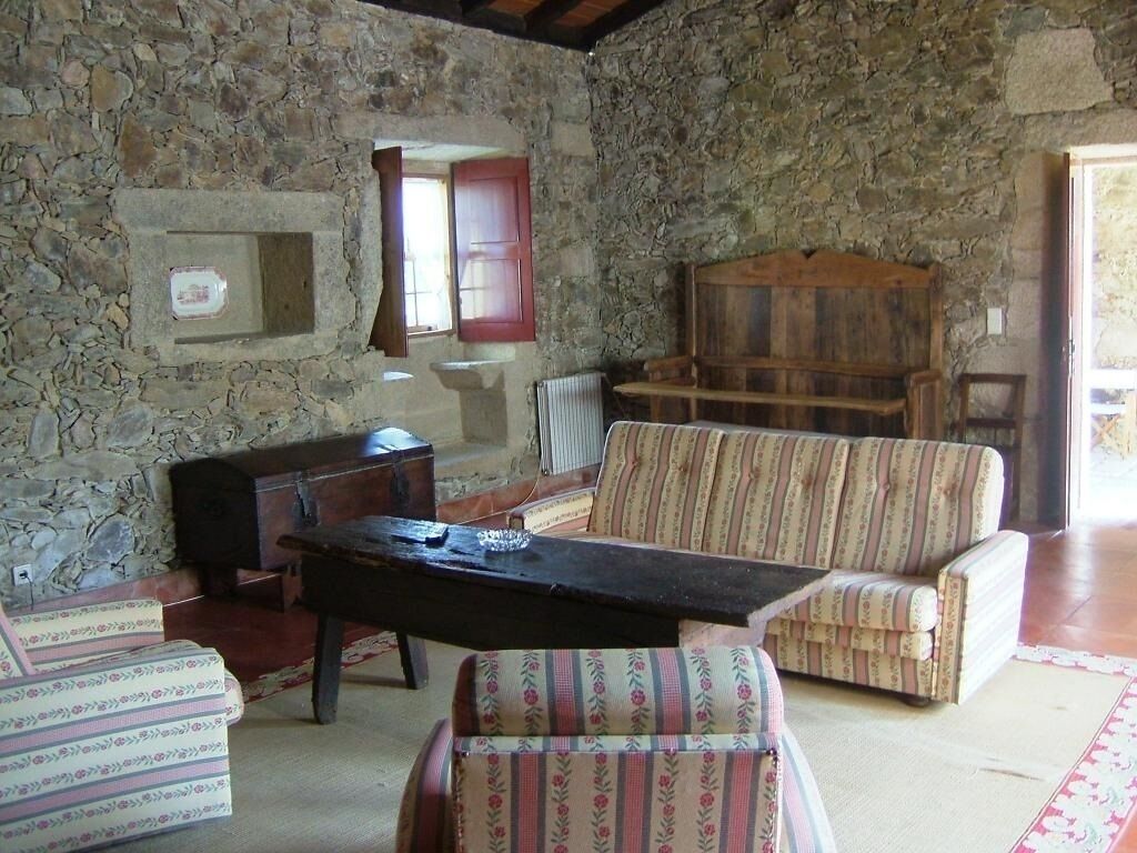 A stone-walled room with a wooden bench, a cushioned armchair, and a small table.