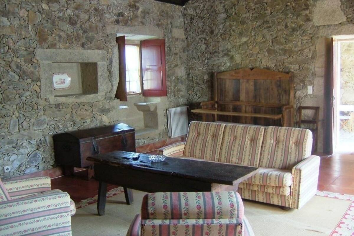 A stone-walled room with a wooden bench, a cushioned armchair, and a small table.