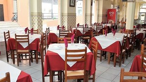 A restaurant with multiple tables covered with red tablecloths and wooden chairs. - Hotel Aliança (Figueira da Foz)