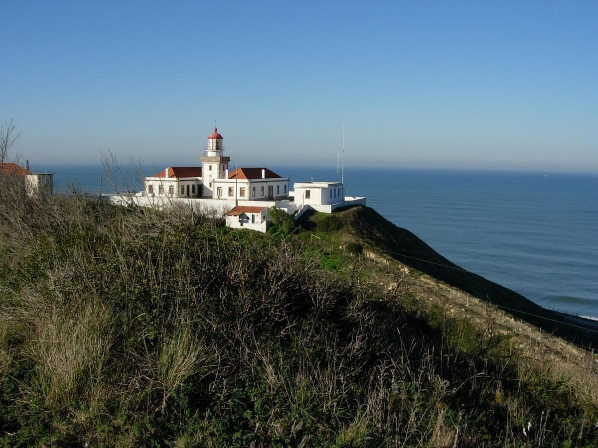 A coastal building with a lighthouse, situated on a grassy hill overlooking the sea.